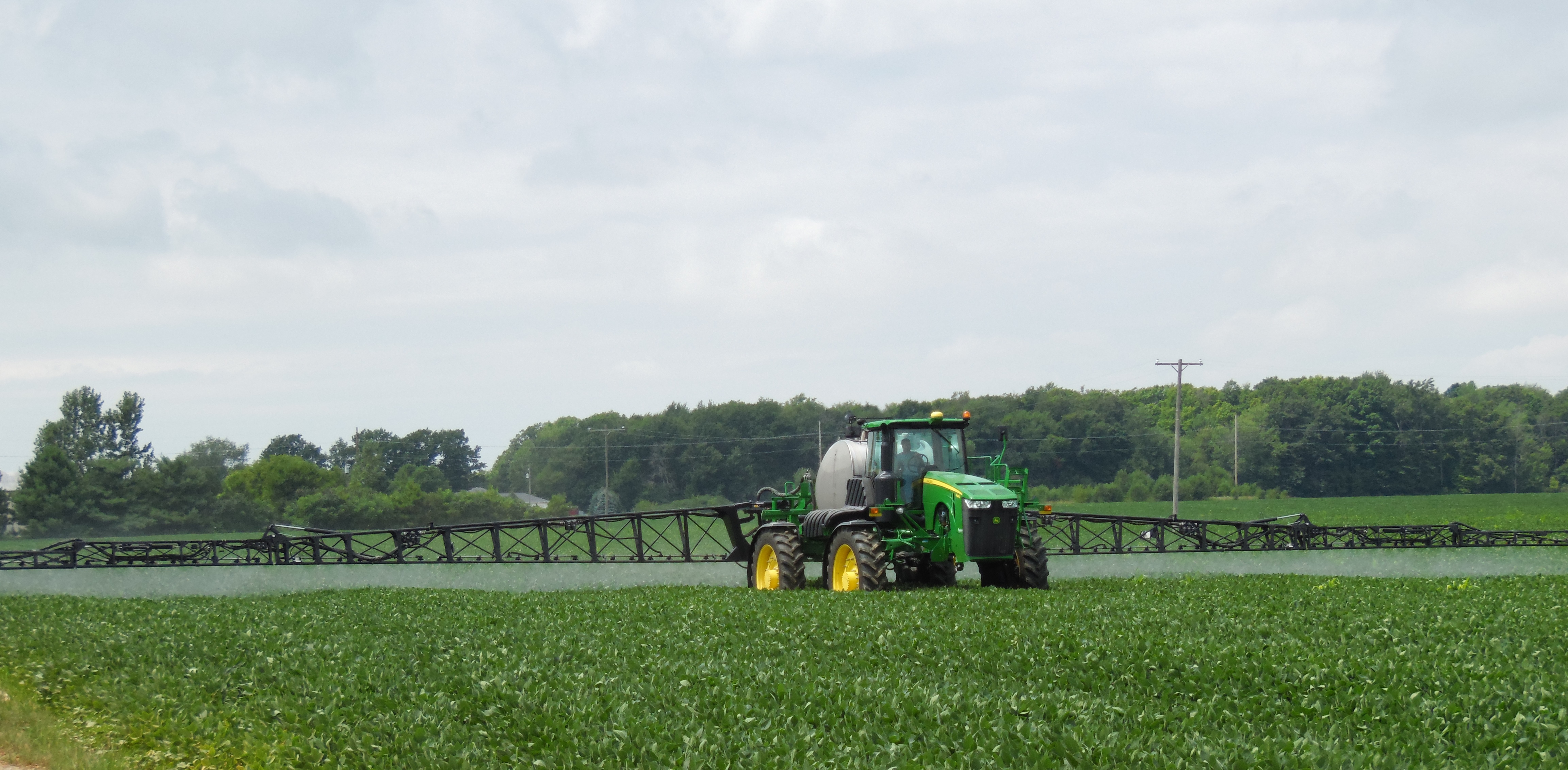 Self-propelled sprayer applying foliar fertilizer in a green soybean field.